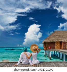 Couple in white on a tropical beach jetty near water villa at Maldives
