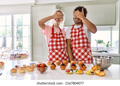 Couple Of Wife And Husband Cooking Pastries At The Kitchen Smiling And Laughing With Hand On Face Covering Eyes For Surprise. Blind Concept. 