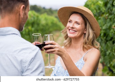 Couple Of Winegrowers Drinking Wine In Vineyard. Close Up Face Of Happy Smiling Woman With Straw Hat Toasting Whit Her Husband. Mature Couple Tasting Wine In Vineyard.