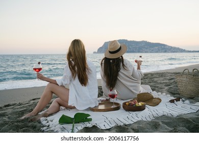 Couple of woman enjoying seaside view, drinking wine alone. Portrait of happy people spending time picnic leisure together on the sunset. - Powered by Shutterstock