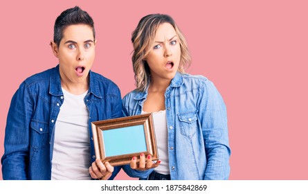 Couple Of Women Holding Empty Frame In Shock Face, Looking Skeptical And Sarcastic, Surprised With Open Mouth 