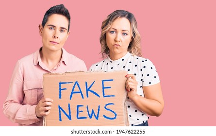 Couple Of Women Holding Fake News Banner Thinking Attitude And Sober Expression Looking Self Confident 