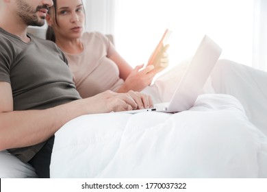 Couple Working From Bedroom, Man Using Laptop Computer, Woman Using Digital Tablet During Lying On Bed, Searching Information And Online Shopping, Social Media For Online Business, Work Form Home