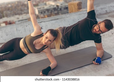 Couple working out on a building rooftop terrace, doing a side plank exercise