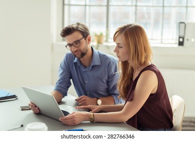 Couple Working Together In An Office Sitting At A Laptop Computer Reading The Screen With Serious Expressions