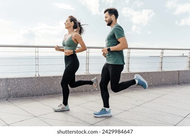 A couple in workout gear run along a waterfront promenade, enjoying fitness with a scenic sea view. - Powered by Shutterstock