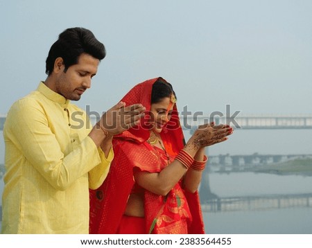 A couple worshipping Lord Sun at sunrise and celebrating the Chhath Pooja - auspicious day, Bihari family, Bihar. A man and a woman in chhath pooja attire praying to God Sun, celebrated in West Ben...