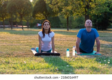 Couple Yoga On Green Grass Outdoor. Yoga Class. Joyful Peaceful People Practicing Yoga Outdoors. Happy Healthy Couple In Yoga Position. Meditation Concentration Peaceful Serene Relaxation Concept