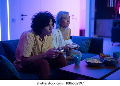 Couple of young adults playing video games at home. Emotional diverse gamers holding joysticks and compete in intense video game on gaming console.