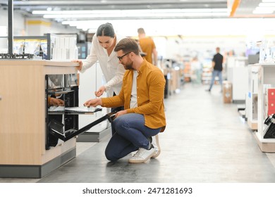 Couple of young customers looking at buildin cookers in domestic appliances shop.