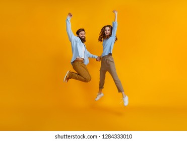 couple of young emotional people man and woman jumping on yellow background