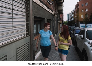 Couple Of Young Friends, Happily Walking Home Together On The City Street At Night. Young Girls In The City Sharing Free Time While Gossiping. Concept Of Friendship And Companionship.