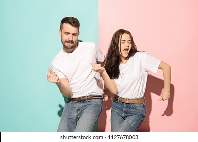 A couple of young funny and happy man and woman dancing hip-hop at studio on blue and pink trendy color background. Human emotions, youth, love and lifestyle concept