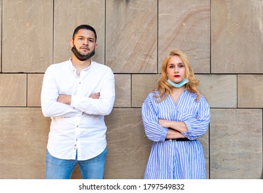 A Couple Of Young Generation Y, Wearing The Mask Of Protection From Infection Under The Chin, Serious Expression And Arms Crossed, The World Pandemic Has Stolen Their Smile