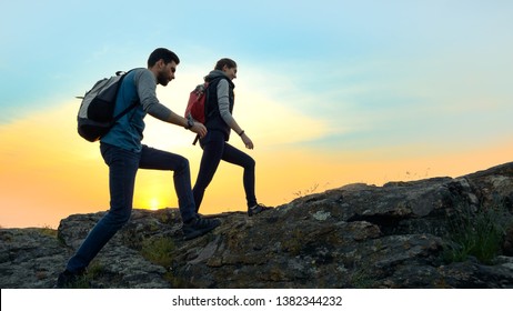 Couple of Young Happy Travelers Hiking with Backpacks on the Beautiful Rocky Trail at Warm Summer Sunset. Family Travel and Adventure Concept.