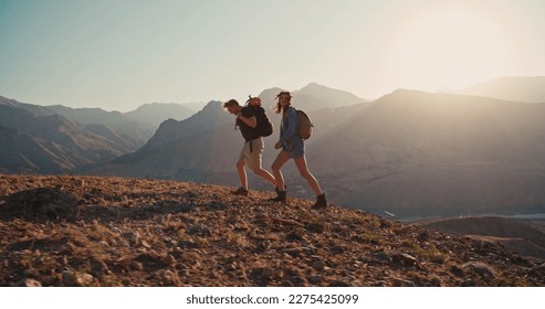 Couple of Young Happy Travelers Hiking with Backpacks on the Beautiful Rocky Trail at Warm Sunny Evening. Family Travel and Adventure Concept. - Powered by Shutterstock