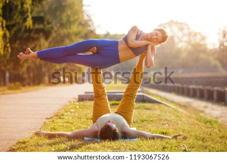 Couple of young man and woman practicing acro yoga in city park