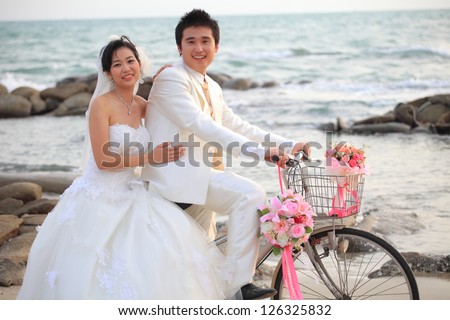 couple of young man and woman in wedding suit riding old bicycle on sand beach