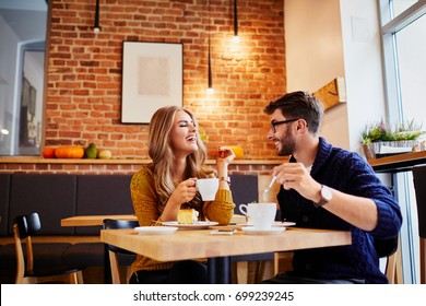 Couple of young people drinking coffee and eating cake in a stylish modern cafeteria