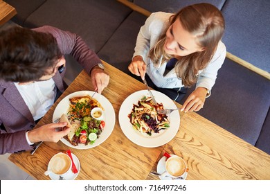 Couple of young people eating breakfast together while sitting in restaurant and smiling
