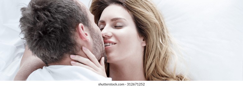 Couple of young people is kissing while lying in bed