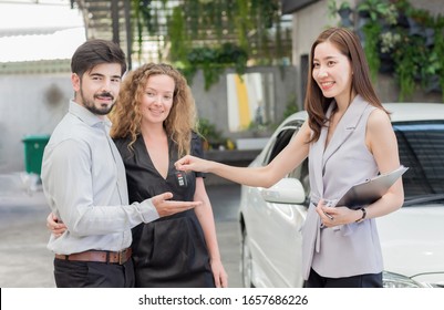 Couple Young Pick Up Car Keys From A Sales Representative In The Car Dealership