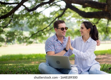 Ein paar junge Teenager, die den Laptop-Computer im Park zusammenklatschen und nutzen, Romantik und Freude in Augenblick der Glückszeit, Glücklich und Lächeln