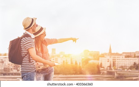 Couple Of Young Tourists Consulting A City Guide Searching Locations In The Street And Pointing - Enjoying The City View