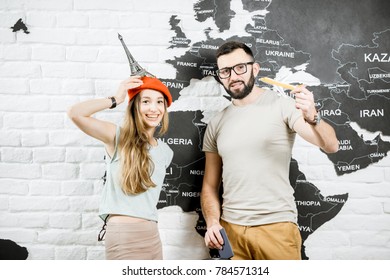 Couple Of A Young Travelers Standing Near The Wall With World Map, Dreaming About A Summer Vacations In Paris