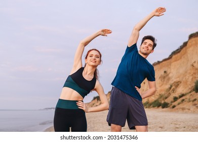 Couple young two friend strong sporty sportswoman sportsman woman man in sport clothes warm up tilt hand body to sides stretch exercise on sand sea ocean beach outdoor seaside in summer day morning