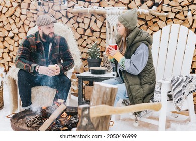 Couple Of Young Woman And Man Having Fun, Tenderness During Teatime Near Fire In Courtyard Of Suburban House In Winter, Concept Of Christmas And New Year Vacation On Farm, Family Love And Support