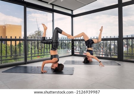 Couple of young women doing yoga poses together in front of studio windows. advanced yoga poses.