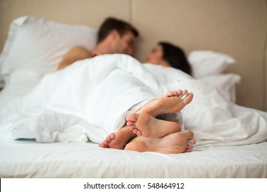 Couple's Feet In Bed. Man With Woman Under Blanket. Rest In Home Comfort.