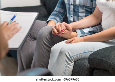 Couples therapy or marriage counseling. Man and woman holding hands on couch during a psychotherapy session. Psychologist, counselor, therapist, psychiatrist or relationship consultant giving advice. 
