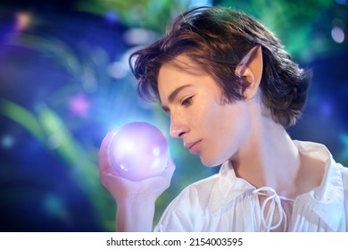 Courageous fairytale elf boy holds a magic sphere of light in his hand while standing in the forest. Fairy tale, magic. Fantasy.