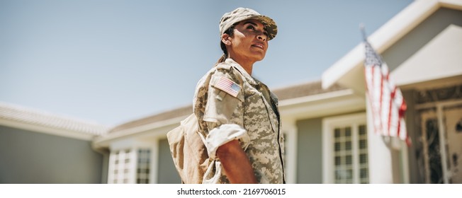 Courageous female soldier looking away thoughtfully while standing outside her house with her bag. American servicewoman coming back home after serving her country in the military. - Shutterstock ID 2169706015