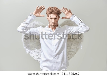 Courageous handsome male Cupid angel in white clothes and with white wings. White background. God of love Cupid. Valentine's Day.