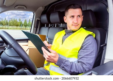 Courier in car. Delivery man in driver's seat. Male courier delivers boxes. Clipboard in hands of delivery man. Postman with boxes. He is engaged in delivery of parcels. Working in postal service