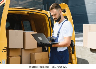 Courier checking orders on a laptop while parked next to a bright yellow delivery van filled with packages, ready for shipping