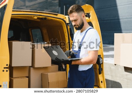 Courier checking orders on a laptop while parked next to a bright yellow delivery van filled with packages, ready for shipping