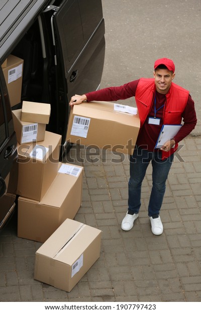 Courier with clipboard and parcel near delivery van\
outdoors, above view