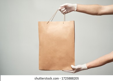 Courier, Delivery Man In Medical Latex Gloves Safely Delivers Online Purchases In Brown Paper Bags To The Door During The Coronavirus Epidemic. Stay Home.