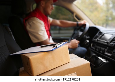 Courier driving delivery van, focus on parcels and clipboard