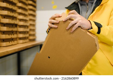 The courier folds a cardboard box against the background of stack of pizza boxes. Brown boxes for shipping and delivery. Many packaging is on the kitchen stock. Food order and delivering concept. - Powered by Shutterstock