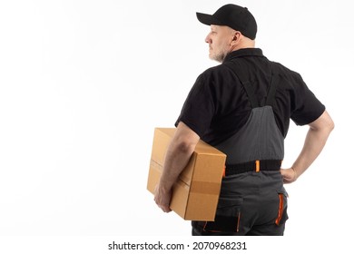 Courier in gray uniform and cap. He holds cardboard box in his hands. Courier stands with his back to camera. Portrait courier with parcel in his hands. Work in order delivery service. Goods delivery