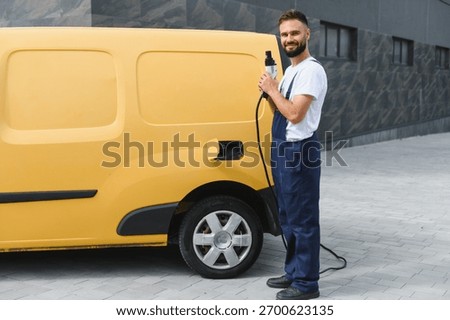 Courier holding a charging cable while powering up an electric delivery van parked on a bustling city street, showcasing sustainable transportation
