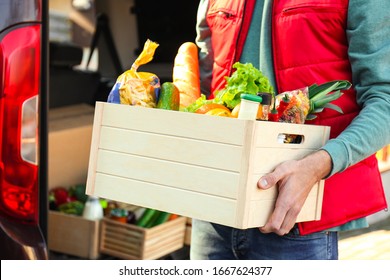 Courier Holding Crate With Products Near Car Outdoors, Closeup. Food Delivery Service