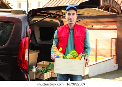 Courier Holding Crate With Products Near Car Outdoors. Food Delivery Service