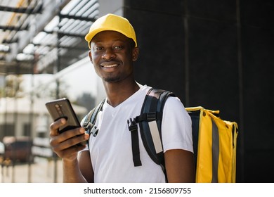 Courier Man With Mobile Phone Looking For Deliver Address Of Food From A Restaurant. African Food Delivery Guy Navigates In Phone In City.