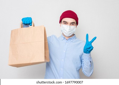 Courier in a medical mask and medical gloves holds a paper bag and symbol peace. Concept of safe delivery. Portrait, mockup